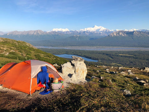 A man and a boy sitting in front of a tent taking in the amazing view of mountains in Alaska