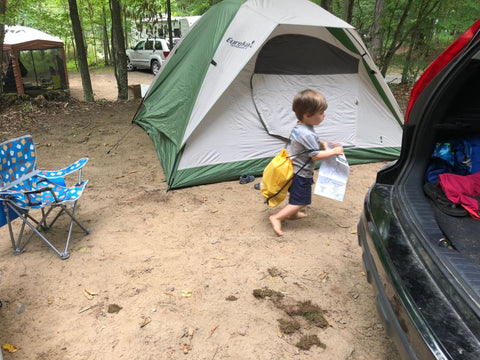 A young boy walking in front of a Eureka tent with other campers in the background