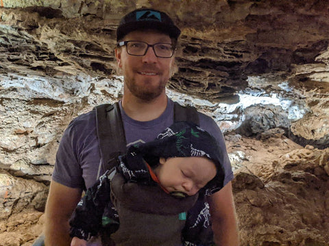 A man wearing a baby in a front-facing carrier while hiking through a cave