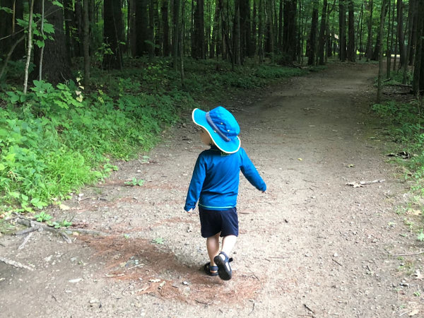 Young boy walking down a trail with a Sunday Afternoons sun hat and a sunshirt on