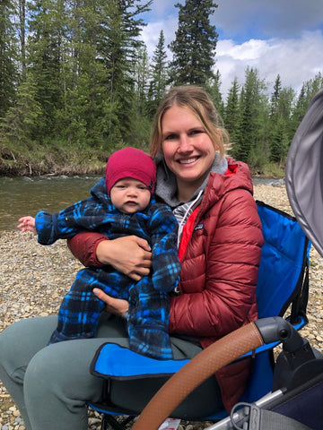 A woman holding a baby while sitting in a camp chair in a wooded outdoor setting