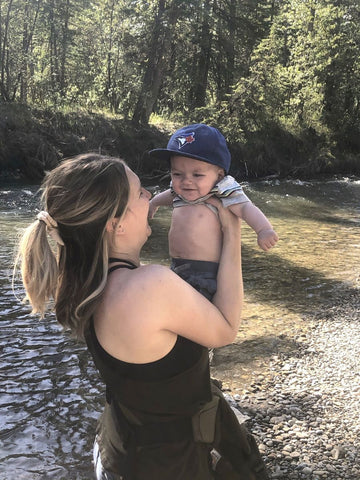 A woman holding up a smiling baby next to a rocky river