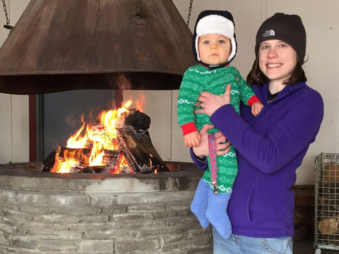 A woman holding a young child in a fleece sleeper inside a warming hut