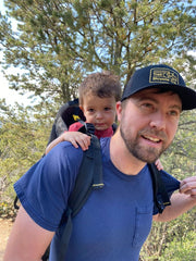 A photo of the author with his son on his back in a framed hiking backpack