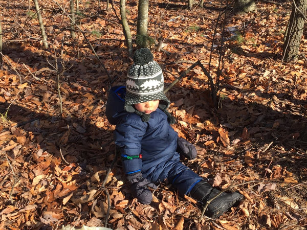 A young boy sitting in the leaves wearing a Columbia snowsuit, winter hat, and winter boots