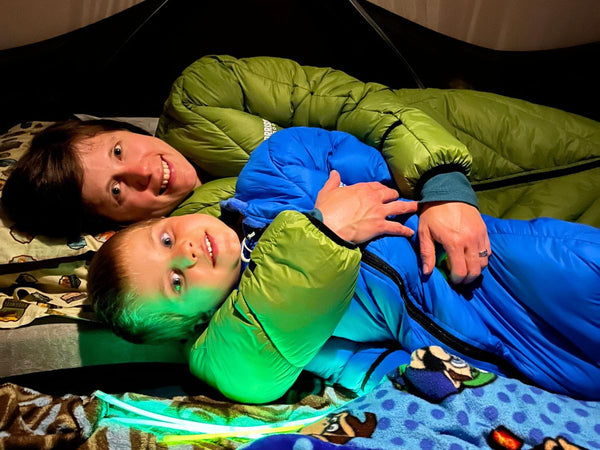 A women snuggling with a boy inside a both, both of them are wearing Morrison Outdoors Sleeping Bags