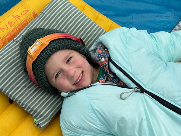 A child wearing a Biolite Headlamp 425 and a Morrison Outdoors Sleeping Bag inside a tent