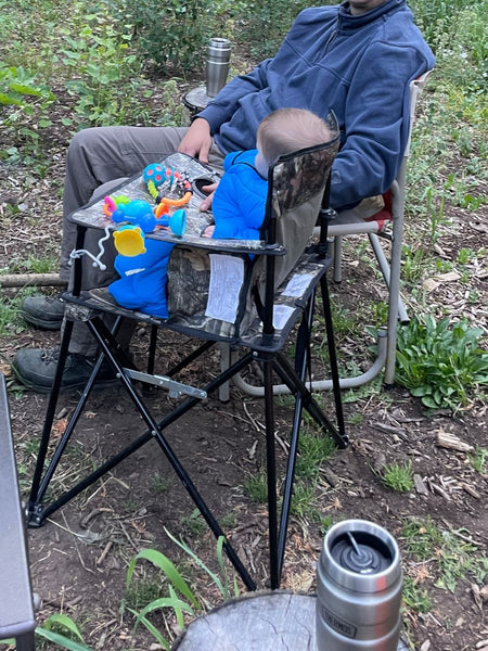 A baby sitting in a camp chair wearing a Morrison Outdoors Little Mo 40 Sleeping Bag at a campsite