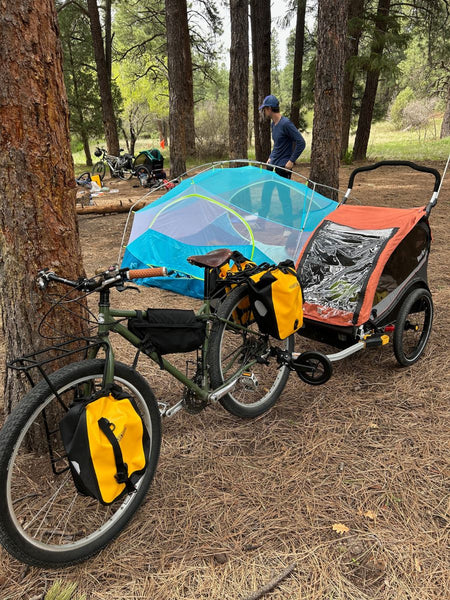 A man setting up a tent near a tree next to a bike with a Burley trailer attached to it