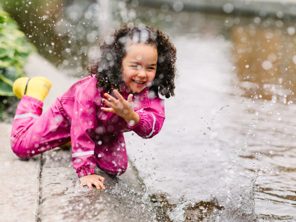 A young girl splashing in puddles while wearing a pink Helly Hansen rain jacket and pants