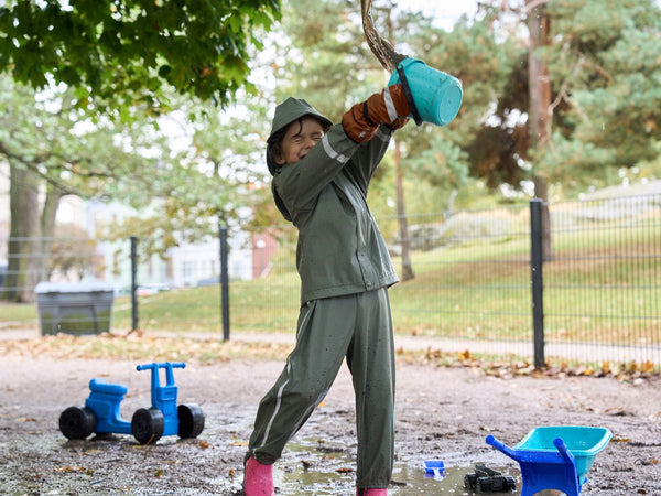 A child playing with water and mud while wearing a Helly Hansen rain jacket and pants and wearing waterproof gloves