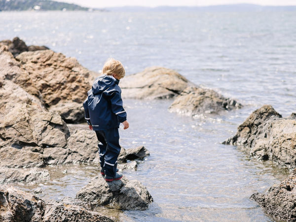 A young child wearing a rainsuit while playing on rocks along a coastline