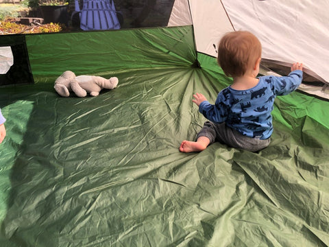 A baby playing in a tent set up in a backyard