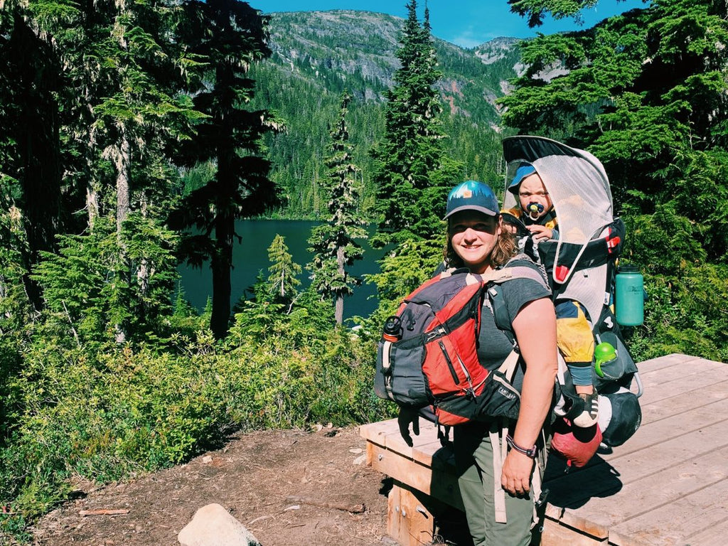 A woman backpacking with a young child in an Osprey Poco framed child carrier