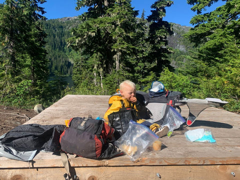 A toddler sitting next to an Osprey Poco framed carrier on a wooden camping platform