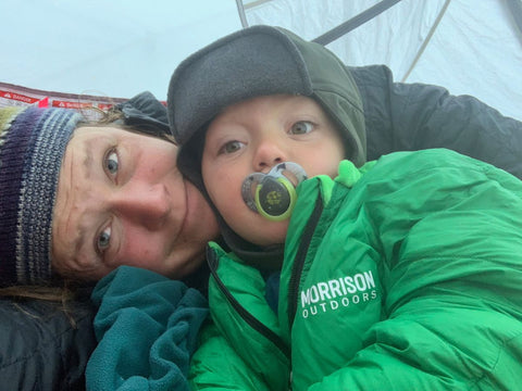 A woman snuggling a toddler wearing a green Morrison Outdoors Big Mo sleeping bag