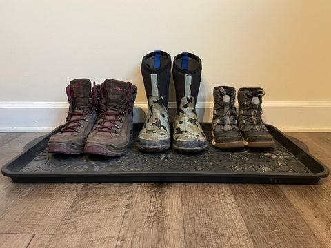 Winter boots lined up on a mat including women's Lowa Renegade boots, kids Bogs boots, and kids Merrell boots